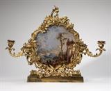 Lot# 1027 An ormolu & reverse-painted glass girandole Composed of associated parts, the cartouche-shaped rocaille, foliage and flower-decorated frame enclosing a coastal scene with figures and a classical ruin, flanked on each side by double S-form foliate candle arms with removable drip pans, on a rectangular plinth mounted with a floral clasp, the reverse with a floral-painted plate, 16.75'' H x 21.5'' W x 8.5'' D, est: $1000/1500