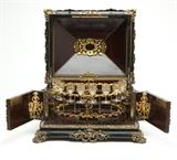 Lot# 1037 A Continental gilt bronze-mounted tantalus Late 19th / early 20th century, the exterior of ebonized wood, the rectangular domed hinged top surmounted by a figural finial depicting a satyr and a nymph, over the double handled body with hinged front panel opening to a rosewood-veneered interior with half figures to each corner and fitted with a removable gilt stemware holder with eight gilt-decorated cordial glasses, the whole raised on foliate scroll feet, 16.5'' H x 18.75'' W x 15.25'' D, est: $1500/2500