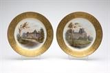 Lot# 1062 Two Sevres style porcelain plates Mid - late 19th century, each with green printed mark ''S. 48.'', each signed ''Guillon'', the first titled ''Tuileries: Pavillon de Flore'', the second titled ''Chateau de la Malmaison'', each circular with a gilt border of scrolling foliage and trophies within reserves surrounding a depiction of a chateau in a landscape painted on a white ground, 2 pcs, each 1'' H x 9.5'' Dia., est: $300/500
