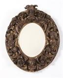 Lot# 1075 A Baroque style carved giltwood mirror Early 20th century, the beveled oval mirror plate within a surround of deeply carved scrolling foliage, flowers and male and female masks applied to a flat base, 28'' H x 23.5'' W x 6.5'' D, est: $600/900
