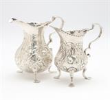 Lot# 1088 Two English sterling silver cream jugs Each London, the first: with partially obscured date mark ''n'' or ''u'' and maker's mark ''S.M'', decorated with rocaille, ''C''-scrolls and fruit; the second: lacking date mark, with crowned leopard's head and maker's mark ''TA'', decorated with foliage, flowers and ''C''-scrolls, 2 pcs, the first 3.75''H x 4''W x 2.5''D; the second 3.625'' H x 3.75'' W x 2.25'' D, 5.5 oz troy tw approximately, est: $400/600