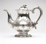 Lot# 1089 A George IV sterling silver teapot
 
1829, London, maker's mark of Joseph Angell, the domed hinged lid with floral finial, joined by a foliage and grape cluster-decorated scrolled handle to the lobed, inverted pear-shaped body, the panels chased and repousse-decorated with floral sprays, scrolls and shell clasps, with a protruding blossom to each rib, issuing a floral-decorated leaf-tip spout and raised on a conformingly decorated domed circular foot, engraved to front and back with an armorial crest and monogrammed ''JL''(?), and with engraved inscription to underside ''To the Memory of the Late General John Calcraft'', 8.25'' H x 10.5'' W x 6'' D, gross weight 30.4 oz troy approximately, est: $800/1000