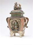 Lot# 1112 A Japanese Satsuma earthenware koro / censer Meiji era (1868 - 1912), with eight-character signature to cover, the rectangular domed pierced cover surmounted by a dog and a rock formation with flowers, the double-handled body with angled corners, one side with a concave niche containing a three dimensional figure of a woman holding a flower and standing on rocks, with blossoming branches painted on the wall behind her, the reverse side painted with a bird and flower sprays, raised on mask-headed paw feet, the whole polychrome-enameled and gilt, 16'' H x 10'' W x 5.5'' D, est: $700/900