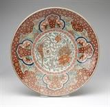Lot# 1114 A large Japanese Imari porcelain charger First quarter 20th century, six-character mark to underside, of shallow circular form, polychrome-enameled and gilt to interior with a central medallion containing a bird and flowers, surrounded by a paneled floral border, the exterior with blue-glazed foliage over a saw tooth border, 3.5'' H x 18'' Dia., est: $400/600