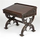 Lot# 1147 A Gothic style oak writing desk Circa 1900, the slant top over two frieze drawers inscribed ''In Domino Confido'' (In God I Trust), the side panels inscribed ''I Can if I Try'' and decorated with foliage, raised on ''X''-form supports joined by a stretcher, on casters, 34.5'' H x 39'' W x 26'' D, est: $400/800