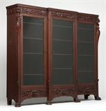 Lot# 1149 An American carved mahogany breakfront bookcase Early 20th century, Grand Rapids, MI, with Grand Rapids Furniture Manufacturers Association label, and stamped ''4301'', the molded cornice over a foliate scroll frieze centering a lion's mask, with lion's mask-headed foliate scrolls to each end, the central glazed door flanked by two further glazed doors, each enclosing four adjustable wooden shelves, above three drawers, each faced with a lion's mask issuing foliage, raised on foliate paw feet, 66.25'' H x 78'' W x 16.5'' D, est: $1000/2000