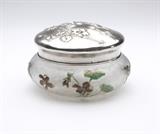 Lot# 1164 A silver-mounted Emile Galle glass powder jar Circa 1900, etched to base ''Cristallerie de Emile Galle Nancy / depose / ex. 1900'' and with further inscription ''Cristallerie de Galle'', the rim and cover each with first standard Minerva mark and maker's mark of Henri Soufflot, Paris, the compressed circular body acid-etched and enameled with iris blossoms and foliage, the domed cover repousse-decorated with a spray of blossoms, 3.5'' H x 5.25'' Dia., est: $3000/4000
