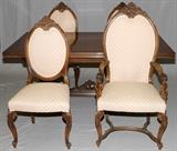 Lot#1065, ITALIAN CARVED WALNUT DINING TABLE, SET OF (6) CHAIRS & COURT CUPBOARD, C. 1930.Including 1 refectory table, H.29 1/2" x 72" (closed) x 42", 2 armchairs and 4 side chairs with peach color fabric upholstery, and 1 court cupboard, H.62" x 40" x 21".  Chairs have carved scrolling leaf crests, seated cherubs carved into arms, cabriole legs terminating in scrolled feet, joined by stretcher.  Table has seated seminude female figures supporting reeded and scroll leaf boat form, centered by carved relief swans, on bun feet.  With table pads.