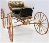 Lot#1, DURANT-DORT CARRIAGE COMPANY "BLUE RIBBON" CARRIAGE, CIRCA 1900. H 62", L 104", D 59"A brass plaque on the back of the seat identifies the "BLUE RIBBON" Carriage, Durant-Dort Carriage Company, Flint Michigan".  Having wood wheels with iron tires attached to the rims and a metal seat with black tufted leather back rest and seat cushion.  Accompanied by a yoke L 90", D 45".