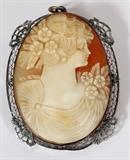 Lot#40, CARVED CAMEO BROOCH, H 2", W 1 1/2"carved cameo of young woman with flowers in hair and shoulder, mounted in a plated filigree frame.