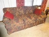 A couch with a decorative pattern and two red throw pillows.