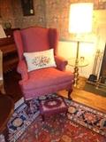 A red upholstered chair with a white throw pillow and matching ottoman.