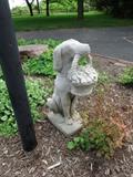 A concrete statue of a dog holding a flower basket.