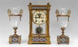 Lot 1001:  ANSONIA CHAMPLEVE CLOCK GARNITURE SET: 3 piece total to include a brass case crystal regulator clock by the Ansonia Clock Co., New York. Case with beveled glass sides, column corners, champleve enamel borders. Porcelain dial marked Ansonia, time and gong strike movement. Overall measures 13 1/4'' h. x 7 1/4'' x 6''. Sold with matching cut glass urn garniture set with champleve enamel inserts, 11 3/4'' h. x 5''.
CONDITION: Uneven finish to brass finish, pendulum appear to be replacement, currently running however not guaranteed to continue.