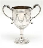 Lot 1134A:  1804 MOSES BRENT ENGLISH STERLING SILVER LOVING CUP: George III period, hallmarked 1804 London and makers mark for Moses Brent. Double handle loving cup or trophy embossed swags on body with gadroon lower bowl, vermeil interior. Engraved swags on foot. Overall measures 10 3/4'' h. x 10 1/2'', approx. 24.3 troy oz.
CONDITION: Minor dings, signs of use.
