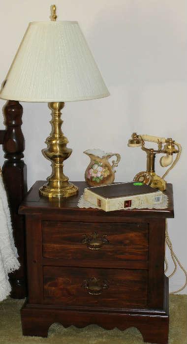 Pine end table that goes with bed with gold and white telephone, lamp, pitcher, and Bible.