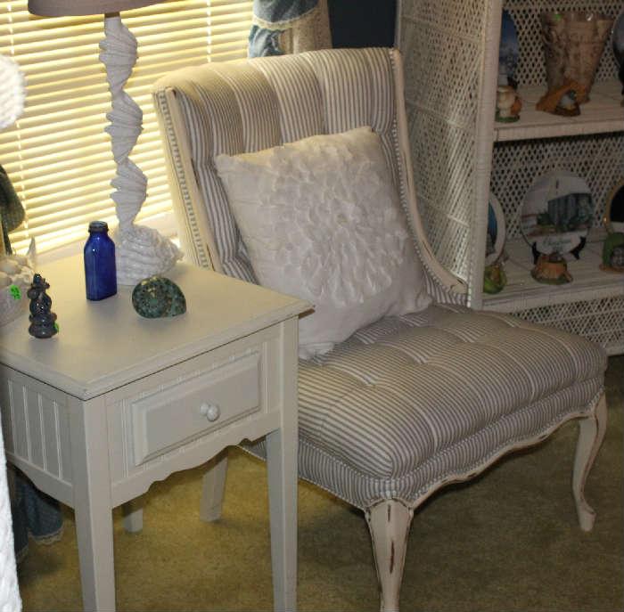 Distressed white chair with mattress ticking fabric with white table with drawer and white shell lamp.