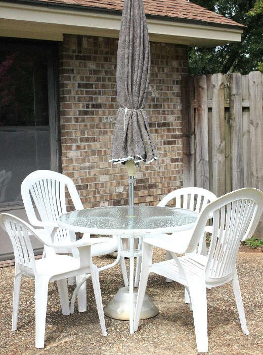 White metal glass top table with umbrella and 4 plastic chairs.