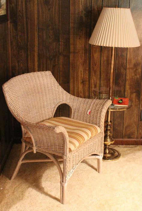 Wicker chair with brown, orange and green stripped cushion with brass floor lamp with glass tray.