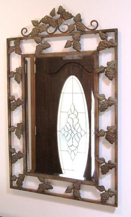 Decorator Mirror with ornate metal frame nicely accented by metal clusters of grapes around its border, beveled mirror (the mirror is showing a reflection of the door panels opposite it)
