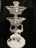 Vista Alegre two tier centerpiece features a whimsical Chinese Man crouching and supporting two tiers of graduated, reticulated porcelain baskets surmounted by a small flower vase.