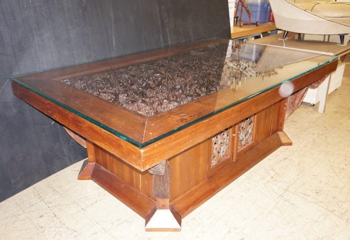 Lot 591  -  Massive Carved Wood Dining Table. Center with Relief Carved Thai Figures: Dancers, deer, etc. Large wood base with two carved doors. Carved bracket supports. 3/4" thick Glass Top.  -- Dimensions:  H: 34 inches: D: 58 inches: L: 95 inches --- 