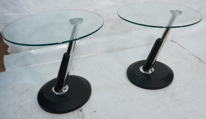 Lot 614  -  Pr Italian style Cantilever Glass Top Chrome Side Tables. Round glass tops on slanted chrome supports with black leather base and trim. -- Dimensions:  H: 22 inches: W: 23.75 inches: D: 23.75 inches --- 