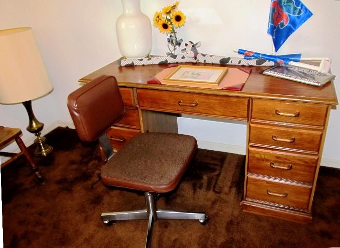Office Desk with light finish,  Right, Left and center drawer storage with brass pulls;  Caster mounted Office Chair with metal pedestal and vinyl seat and back; Accent Table Lamps shown are also available.