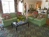 Kitchen/Hearth Area: A CENTURY 85" green sofa and matching 60" love seat (priced separately); black/gold coffee table; various decorative items.  The rug (13'  5" x 13' 7") is a dominant green black design with shades of burgundy and rose.