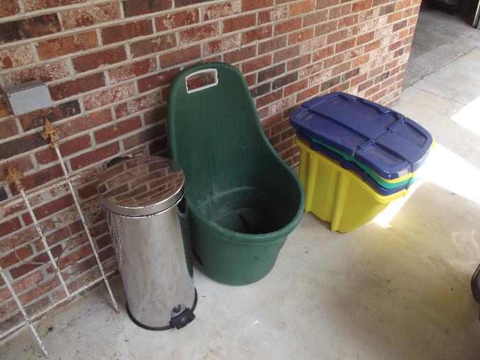 Assortment of storage bins with lids, stainless trash can and verticl wheel barrow. Notice the vintage wrough iron fencing to the left. 