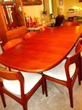 Beautiful Vintage Scan DesignTeak Wood Dining Set... Large oval shaped Teak Dining Table... shown with extra leaf, rich finish, pedestal style base, and unique hideaway for extra leaf; 8 matching teak wood chairs with neutral sculpted upholstery.