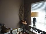 Decorative items, lamps, sofa table, tall flower arrangement in glass vase.