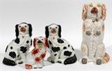 Lot#1112, ENGLISH STAFFORDSHIRE SEATED DOGS, MID 19TH C., FOUR, H 7 1/2"-14 1/2"Including one seated dog with basket of flowers in mouth, one dog seated on its hind legs with pipe in mouth, and a pair of black spotted dogs. Mid 19th Century. Measuring H. 7 1/2" to 14 1/2".