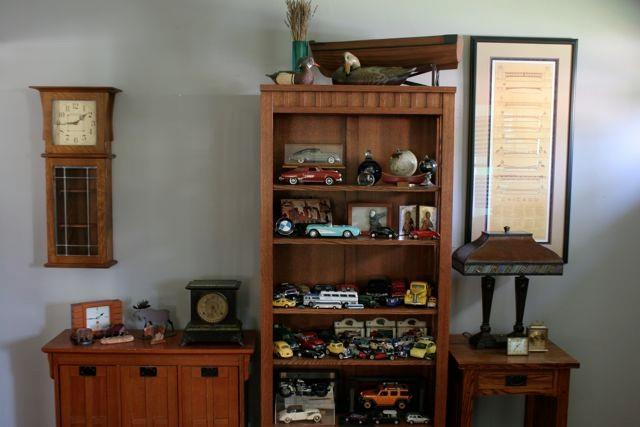 In the entry, open shelving holds a display of model cars, art glass, duck decoys and small artwork. The oak and leaded glass wall clock is by American Craftsman.