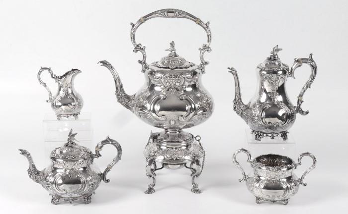 Lot 1005:  5 PIECE ORNATE ENGLISH STERLING SILVER TEA SERVICE: An assembled collection with a matching floral repousse motif to include 1) 1896 Charles Lamb, Dublin, hot water kettle on stand. Hinged lid with eagle finial, figural masqueron and bird head on spout. Paul Storr, London, 1815 marked burner. Overall 19 1/4'' h. x 12''. 2) 1920 William Gibson & John Langman, ''Goldsmiths & Silversmiths Co.'', London, coffee pot. Hinged lid with eagle final, matching spout, 10'' h. x 9 3/4''. 3) Gibson & Langman teapot, hinged lid with eagle finial, matching spout, 7 1/2'' h. x 10 1/2''. 4) Gibson & Langman open creamer 5 3/4'' h. x 5''. 5) Gibson & Langman open sugar, 5 3/8'' h. x 8 1/2''. Approx. 148.9 troy oz. Est. $6000/8000**
CONDITION: Varying signs of use including minor dings.