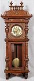 Lot#158, GUSTAV BECKER, GERMAN WALL CLOCK, 19TH C., H 48", W 20"Carved German wall clock by Gustav Becker, mounted with brass ornamentation throughout, and flanked by fluted column forms. Having a three key wind, brass face, with Arabic numerals. Measuring H. 48 1/2" x 20", 19th Century.
