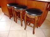 3 CARVED COUNTER STOOLS WITH BLACK LEATHER SEATS/NAILHEAD DETAIL.