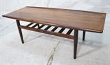 Lot 163:  GRETE JALK Danish Glostrup Rosewood Coffee Table. Flared rolled edges. Lower slat shelf.  Remnant of partial label. : Dimensions:  H: 17 inches: W: 51 inches: D: 21 inches --- 