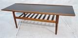 Lot 165:  GRETE JALK Danish Rosewood Coffee Table. Flared rolled edges. Black laminate top. Lower slat shelf.  Tapered peg legs. Not marked: Dimensions:  H: 20 inches: W: 63 inches: D: 23.5 inches --- 