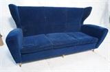 Lot 914:  MELCHIORRE BEGA Retro Blue Three Seater Sofa couch. Wood peg legs. Gio Ponti style. Rich blue fabric upholstery. Tall wide wing back. Not marked. : Dimensions:  H: 40 inches: W: 77 inches: D: 34 inches --- 