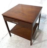 Lot 919:  PAUL McCOBB Calvin Walnut Night Stand. One Drawer Stand with woven bottom. Metal pull. Label. : Dimensions:  H: 24 inches: W: 22 inches: D: 22 inches --- 