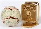 Lot#149, 1894 DETROIT TIGERS TEAM SIGNED, BASEBALL AND GILT METAL MINIATURE WORLD SERIES DESK PLAQUE, 2 PCS. H 4", W 3"includes one Detroit Tiger baseball signed by the 1984 Detroit Tigers, an one miniature gilt metal desk plaque on stand with a home plate base. Plaque pivots on the base and is inscribed with the World Series trophy on one side and "World Champions 'D'(English D) 1984" on opposite side. Baseball is signed by players and coaches including: Jack Morris, Alan Trammell, Lou Whitaker, Kirk Gibson, Lance Parrish, Howard Johnson, Doug Bair, Aurelio Lopez, Dan Petry, Dave Rosema, Milt Wilcox, Marty Castillo, Dave Bergman, Tom Brookens, Barbaro Garbey, Larry Herndon, Ruppert Jones, Chet Lemon, Darrell Evans; Manager Sparky Anderson, Coaches, Billy Consolo, Alex Grammas, Dick Tracewski, Roger Craig. 24 signatures. Plaque presented to Detroit Mayor Coleman A. Young by the Detroit Tigers. Consigner purchased from the Coleman A. Young estate sale.