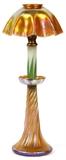 Lot#1001, L. C. TIFFANY GOLD FAVRILE GLASS CANDLESTICK LAMP, EARLY 20TH C., H 18"Candlestick lamp by Louis Comfort Tiffany, featuring a gold favrile glass base and shade. Signed, "L.C.T.". Measuring H. 18" overall, with the base measuring H. 9 1/4", and the shade measuring H. 3 3/8" x 6 1/2". Early 20th Century.