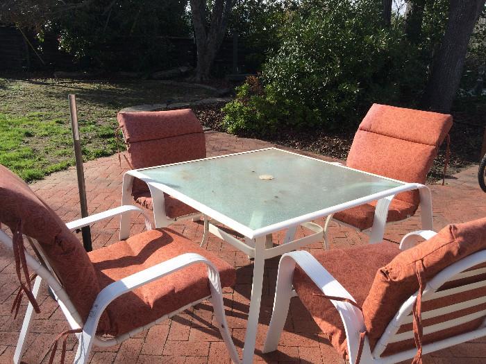 Glass Patio Table with 4 White Chairs and 4 Orange Cushions. Umbrella Stand.