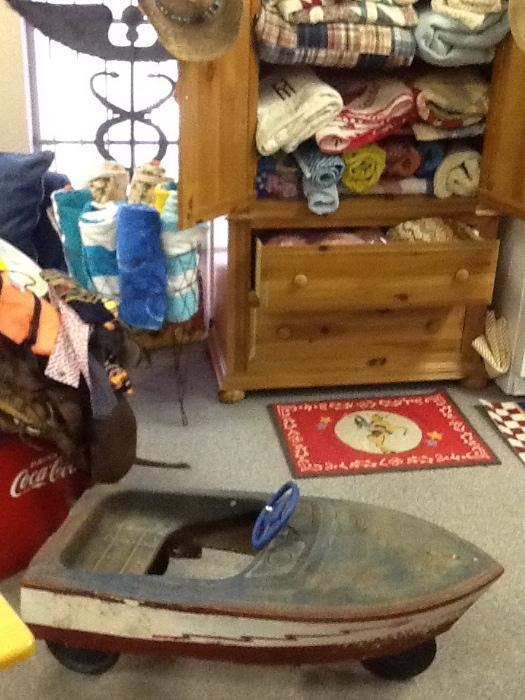 Forged steel medical sign (2x5) hanging; misc comforters and beach towels; antique Murray pedal boat; cowgirl throw rug; basket stand w beach towels; cabinet holding comforter is boyhill; saddle w blanket on coke chest;