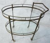 Lot 688:  Oval Brass Rolling Tea Bar Cart. Vintage Modern. Two glass shelves.: Dimensions:  H: 31 inches: W: 29.75 inches: D: 21.5 inches --- 