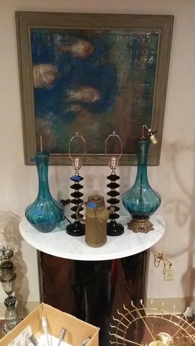 A lovely underwater vignette of original oil painting, Italian art glass lamps, atop a black, wooden/white marble-topped demilune table.