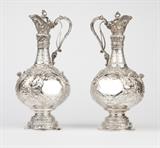 1136  A pair of Victorian sterling silver ewers, Walter & John Barnard
1892 & 1894, London, each with maker's mark, one further marked ''967'', the other ''776'', each all-over chased and repousse-decorated in high relief with rocaille, floral garlands, margents and masks, each hinged lid surmounted by a tripartite rocaille finial and opened via a trigger mechanism attached to the interior of the neck-mounted scroll handle, the slender tapering neck over a squat body decorated to two sides with a shaped reserve flanked by merfolk with applied wings, heads, and outstretched hands, centered by a single applied lion's head, raised on a domed and stepped circular foot, one: 14.5'' H; the other: 14.75'' H x 6.5'' Dia., gross weight 84.25 oz troy approximately, est: $15,000/25,000

Provenance: Private Collection, La Jolla, CA.  Condition: Overall good condition. Not monogrammed. General light marks, rubbing, and tarnishing commensurate with age. One with a pin loose to lower section of handl