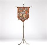 1138  A Victorian beaded needlepoint fire screen on brass stand
Second half 19th century, the needlepoint panel with beaded grey and white calla lilies centering a geometric, banded reserve accented with grey roses, over a rust-colored background with a brown wrapped cord border and ties, suspended from a fleur de lis-surmounted brass standard with an adjustable-height slider, raised overall on three spiral legs terminating in acanthus-topped claw feet, 58.75'' H x 24'' W x 14'' D, est: $600/900

Provenance: Private Collection, La Jolla, CA.  Condition: Overall good condition. Minor sun fading to panel and verso liner and some rippling to panel at bottom edge due to weight of beading commensurate with age. A few scattered beads deficient. Finial to one end of crossbar bent slightly back.  Your bid indicates acceptance of our Conditions of Sale.  AS-IS.  ALL SALES FINAL