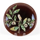 1148  A Majolica Palissy-style wall platter, likely Rafael Bordalo Pinheiro
Early 20th century, impressed to verso ''Made / In / Portugal / (illegible circular mark) / A.V / 18'', circular mark likely that of Rafael Bordalo Pinheiro, the circular brown-glazed plate with an applied polychrome chestnut branch issuing leaves and seed pods; two pods cut away revealing chestnuts inside, centered overall by a perched kestrel , 3'' H x 17.75'' Dia., est: $600/900

Provenance: Private Collection, Encino, CA.  Condition: Overall good condition. Maker's mark lightly impressed and illegible, as stated. Craquelure to glaze throughout. A localized 2'' x 1.5'' area of light scratching to upper plate.  Your bid indicates acceptance of our Conditions of Sale.  AS-IS.  ALL SALES FINAL